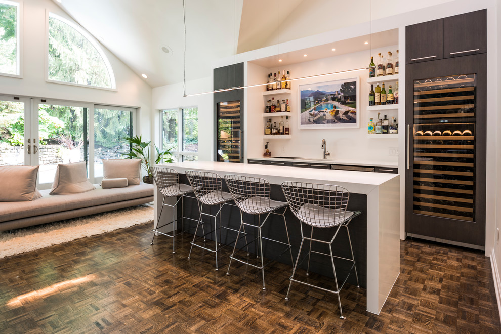 Inspiration for a contemporary galley seated home bar in Cincinnati with flat-panel cabinets, dark wood cabinets, dark hardwood floors, brown floor and white benchtop.