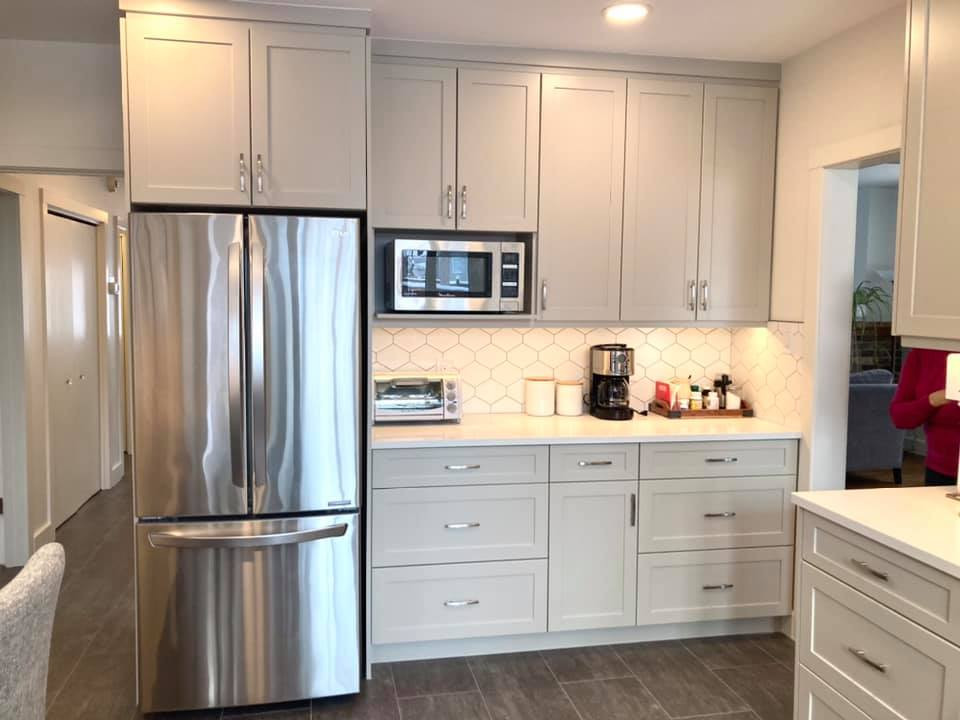 Mid-sized transitional u-shaped vinyl floor and gray floor enclosed kitchen photo with an undermount sink, shaker cabinets, beige cabinets, quartz countertops, white backsplash, ceramic backsplash, stainless steel appliances and white countertops