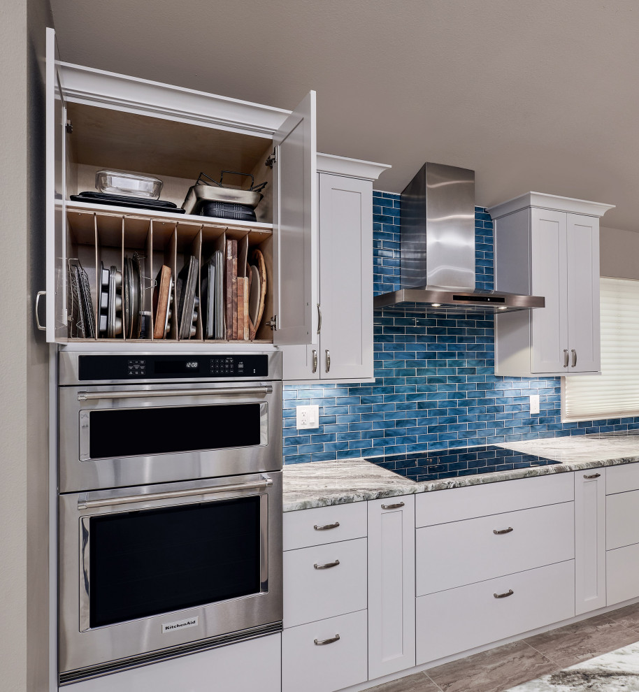 Transitional porcelain tile and gray floor kitchen pantry photo with a triple-bowl sink, shaker cabinets, white cabinets, quartzite countertops, blue backsplash, glass tile backsplash, stainless steel appliances, an island and gray countertops