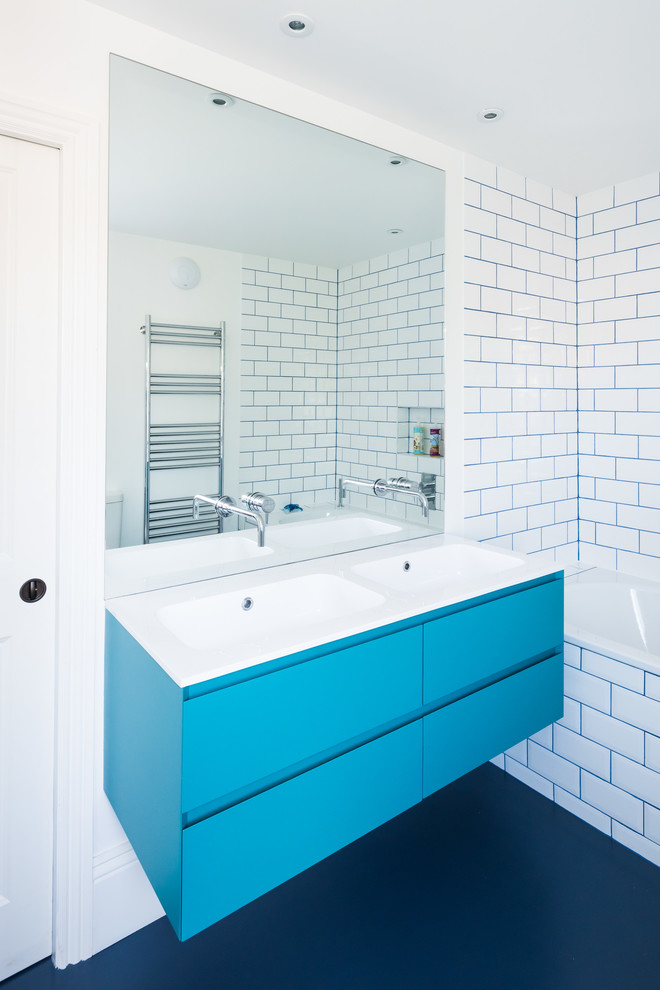 This is an example of a large modern kids bathroom in London with flat-panel cabinets, blue cabinets, a drop-in tub, an open shower, a wall-mount toilet, white tile, porcelain tile, white walls, linoleum floors, an integrated sink, quartzite benchtops, blue floor, a sliding shower screen and white benchtops.