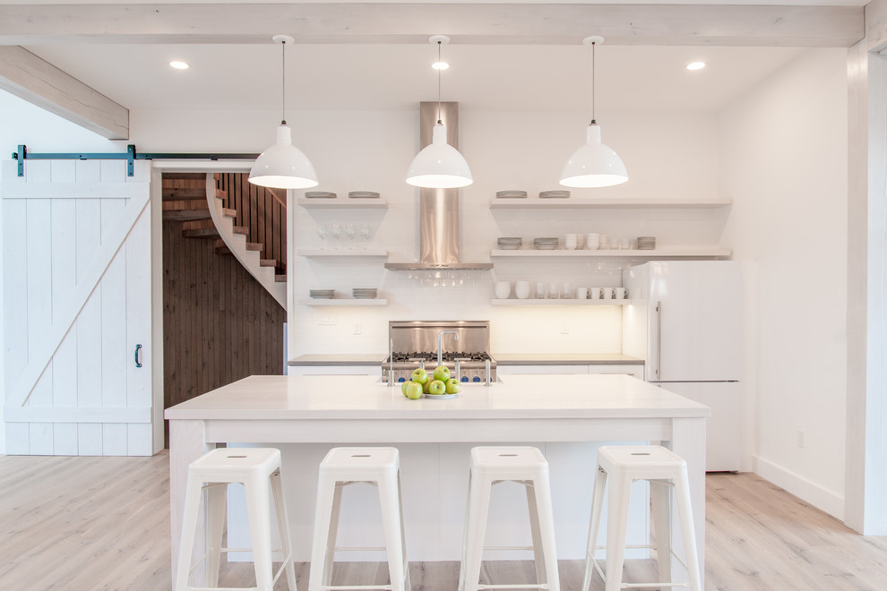 Inspiration for a mid-sized country galley kitchen in Baltimore with open cabinets, white cabinets, stainless steel appliances, light hardwood floors, with island, a farmhouse sink, quartz benchtops, white splashback, porcelain splashback and brown floor.