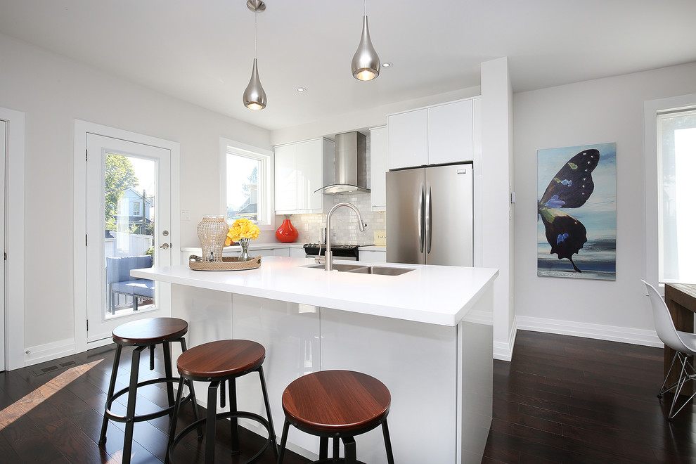 Mid-sized contemporary l-shaped open plan kitchen in Toronto with an undermount sink, flat-panel cabinets, white cabinets, quartz benchtops, beige splashback, stone tile splashback, stainless steel appliances, medium hardwood floors and with island.