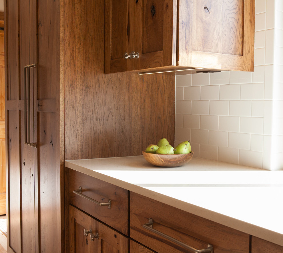 Kitchen - mid-sized rustic l-shaped kitchen idea in Indianapolis with a single-bowl sink, flat-panel cabinets, medium tone wood cabinets, quartz countertops, white backsplash, subway tile backsplash, paneled appliances, white walls and an island