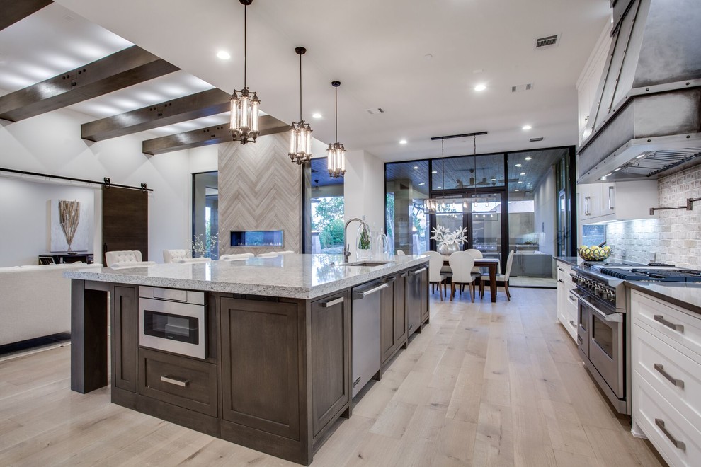 Inspiration for a large transitional l-shaped open plan kitchen in Dallas with an undermount sink, shaker cabinets, white cabinets, granite benchtops, grey splashback, stone tile splashback, stainless steel appliances, medium hardwood floors, with island and brown floor.