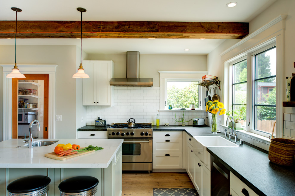 Photo of a mid-sized eclectic l-shaped open plan kitchen in San Francisco with a farmhouse sink, shaker cabinets, white cabinets, soapstone benchtops, white splashback, subway tile splashback, stainless steel appliances, light hardwood floors, with island and brown floor.