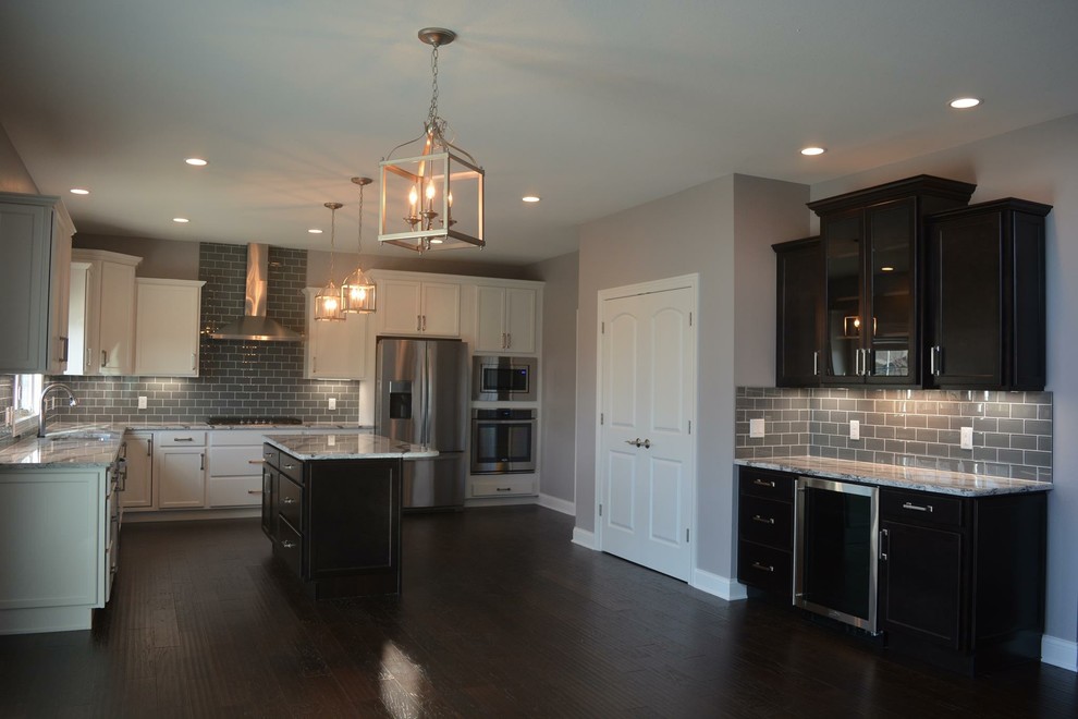 Large transitional l-shaped dark wood floor open concept kitchen photo with an undermount sink, shaker cabinets, white cabinets, granite countertops, gray backsplash, porcelain backsplash, stainless steel appliances and an island