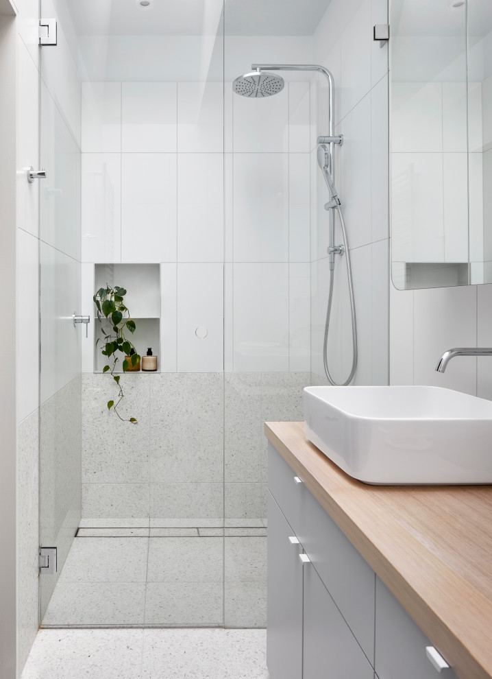 This is an example of a mid-sized contemporary master bathroom in Melbourne with furniture-like cabinets, grey cabinets, a curbless shower, a one-piece toilet, porcelain tile, white walls, terrazzo floors, a vessel sink, wood benchtops, beige floor, a hinged shower door, brown benchtops, a single vanity and a built-in vanity.