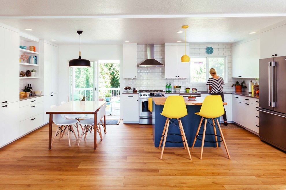 Photo of a mid-sized contemporary l-shaped eat-in kitchen in Portland with an undermount sink, flat-panel cabinets, white cabinets, quartz benchtops, white splashback, subway tile splashback, stainless steel appliances, vinyl floors, with island and brown floor.