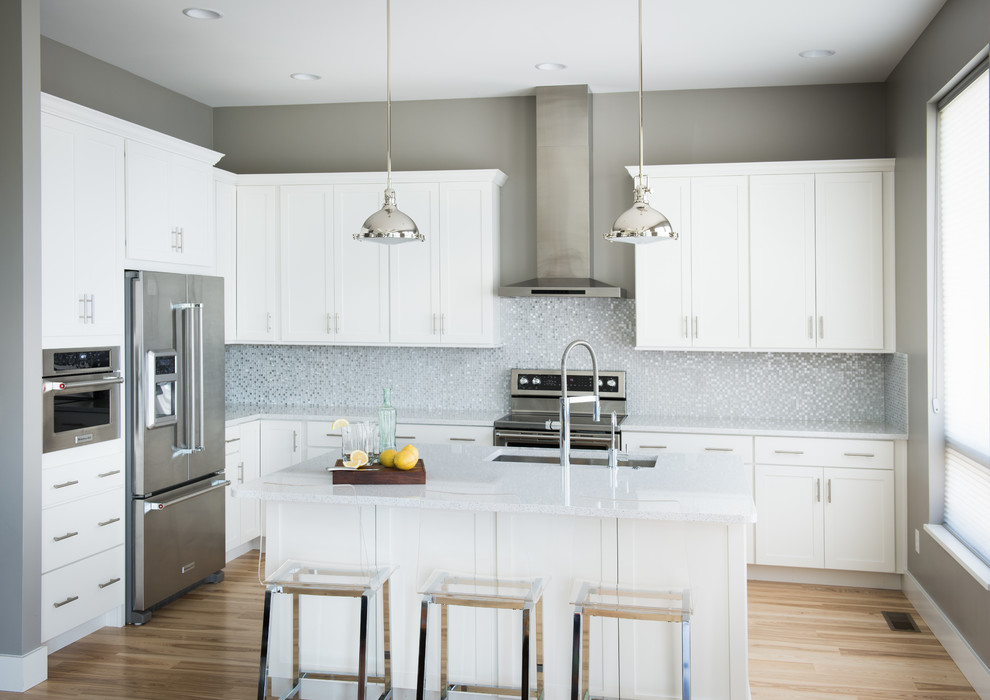 Inspiration for a mid-sized transitional l-shaped light wood floor open concept kitchen remodel with an undermount sink, shaker cabinets, white cabinets, quartz countertops, multicolored backsplash, glass tile backsplash, stainless steel appliances and an island