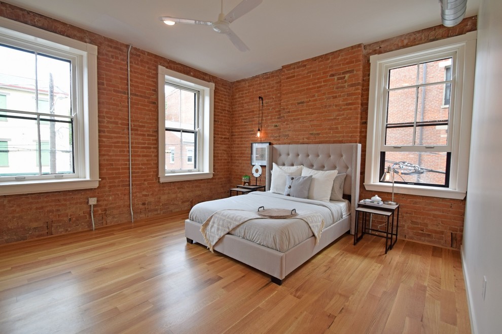 Large industrial master bedroom in Cincinnati with brown walls, light hardwood floors and brown floor.