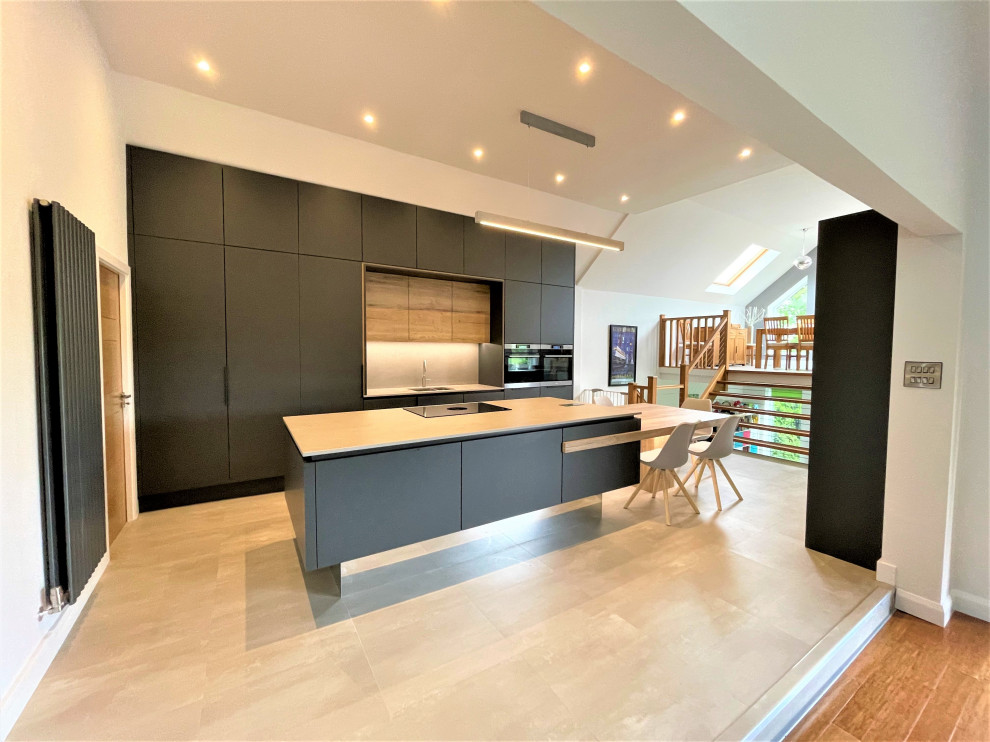 Inspiration for a large contemporary single-wall open plan kitchen in Other with a double-bowl sink, flat-panel cabinets, light wood cabinets, solid surface benchtops, grey splashback, black appliances, vinyl floors, with island, grey floor, grey benchtop and vaulted.