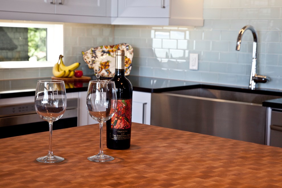 Eat-in kitchen - large transitional l-shaped medium tone wood floor and brown floor eat-in kitchen idea with a farmhouse sink, shaker cabinets, white cabinets, quartzite countertops, blue backsplash, glass sheet backsplash, stainless steel appliances and an island