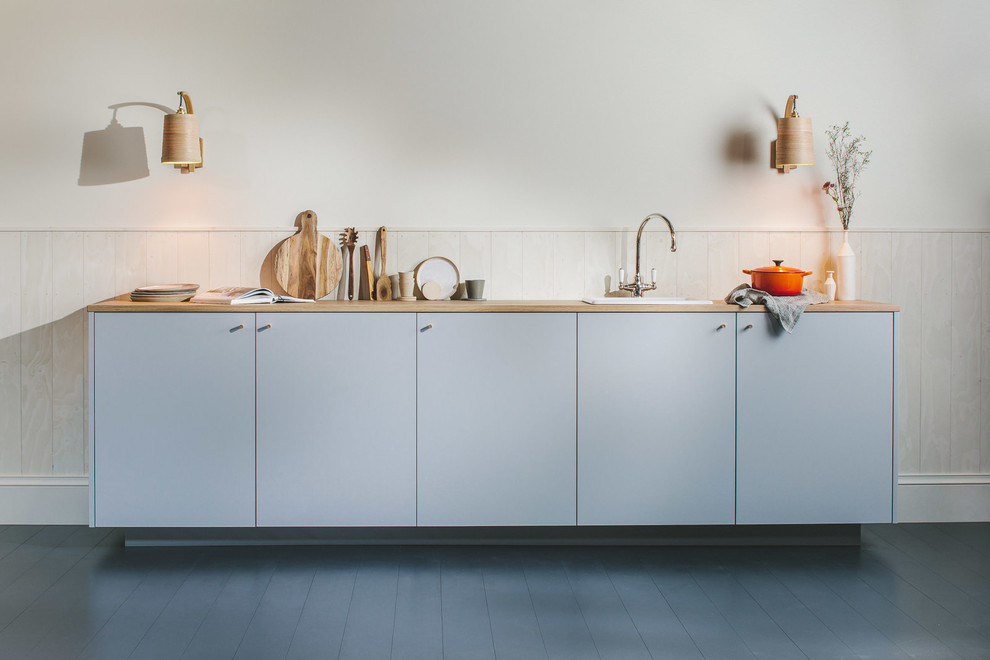 Photo of a small scandinavian single-wall open plan kitchen with a single-bowl sink, flat-panel cabinets, grey cabinets, wood worktops, white splashback, wood splashback, integrated appliances, painted wood flooring, no island, black floors and brown worktops.