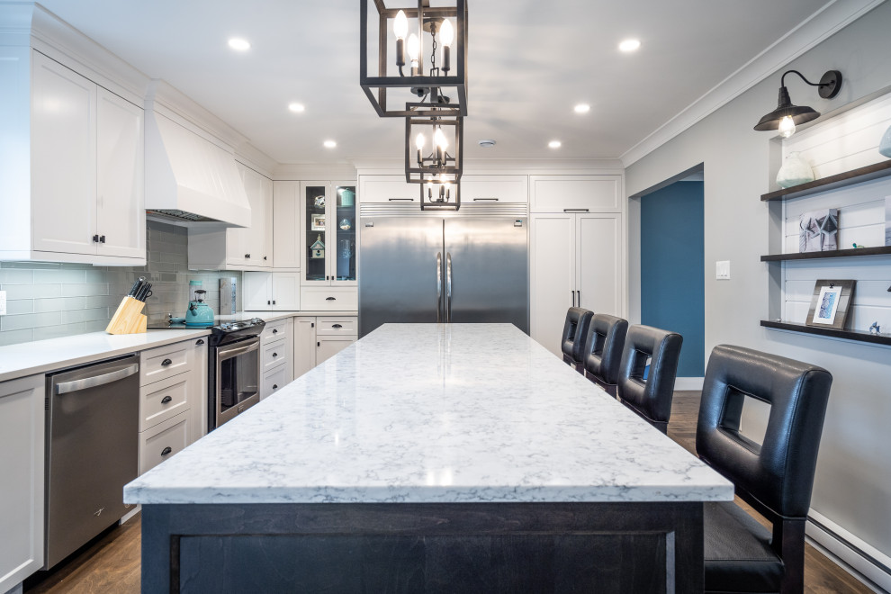 Inspiration for a large transitional l-shaped medium tone wood floor and brown floor kitchen remodel with an undermount sink, white cabinets, quartz countertops, white backsplash, glass tile backsplash, stainless steel appliances, an island and white countertops