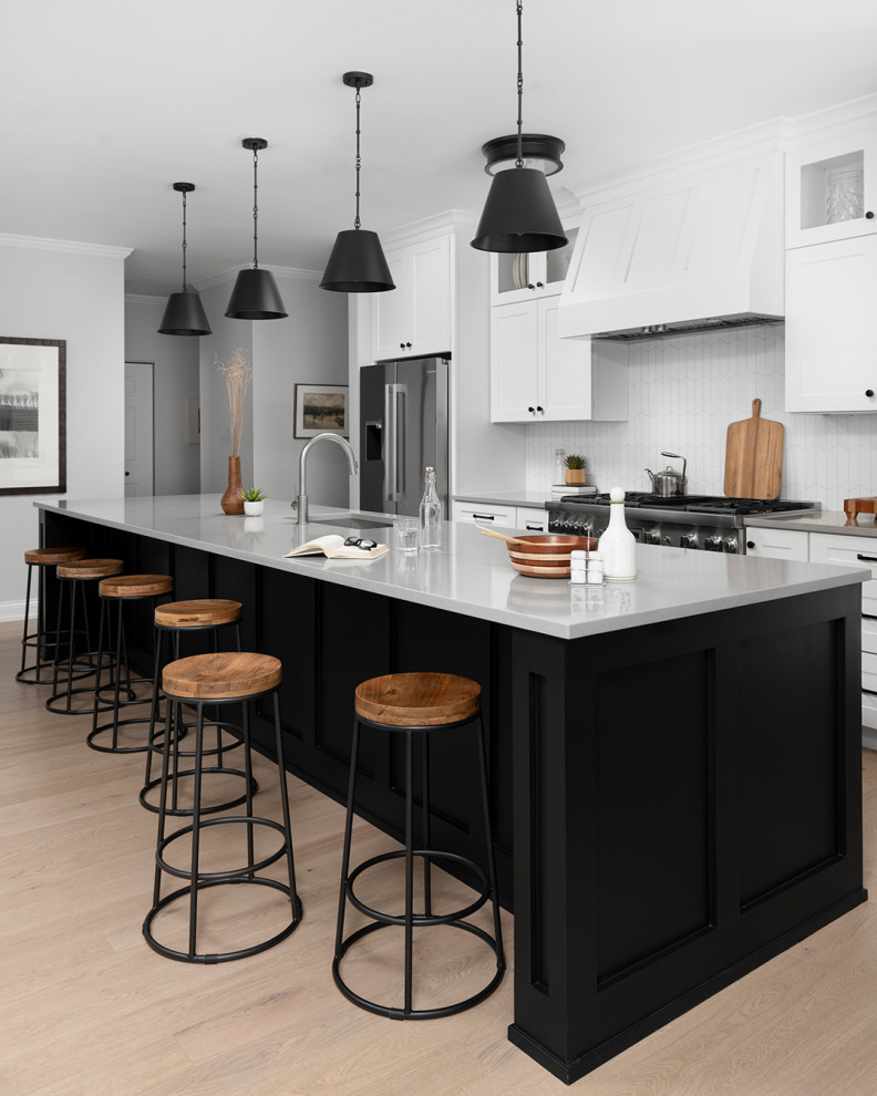Open concept kitchen - mid-sized transitional galley light wood floor open concept kitchen idea in Chicago with an undermount sink, shaker cabinets, white cabinets, quartz countertops, white backsplash, ceramic backsplash, stainless steel appliances, an island and gray countertops