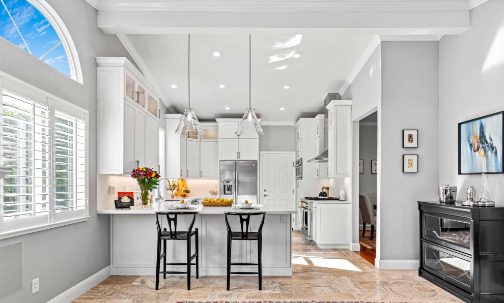 Mid-sized transitional u-shaped open plan kitchen in San Francisco with an undermount sink, recessed-panel cabinets, white cabinets, quartz benchtops, white splashback, marble splashback, stainless steel appliances, limestone floors, a peninsula, beige floor, white benchtop and vaulted.