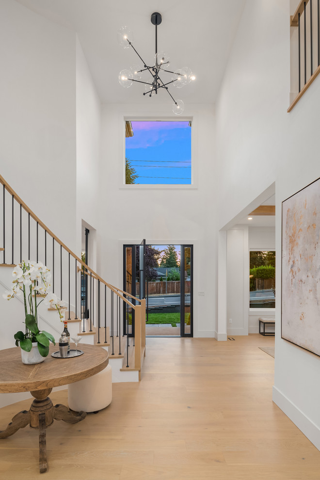 This is an example of a large contemporary foyer in Seattle with white walls, light hardwood floors, a pivot front door and a black front door.