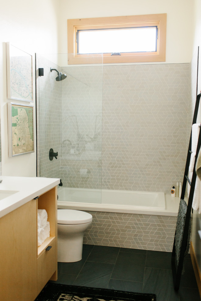 Photo of a mid-sized contemporary 3/4 bathroom in Seattle with flat-panel cabinets, light wood cabinets, a drop-in tub, a shower/bathtub combo, a two-piece toilet, gray tile, mosaic tile, beige walls, ceramic floors, an undermount sink, solid surface benchtops, black floor, an open shower and white benchtops.
