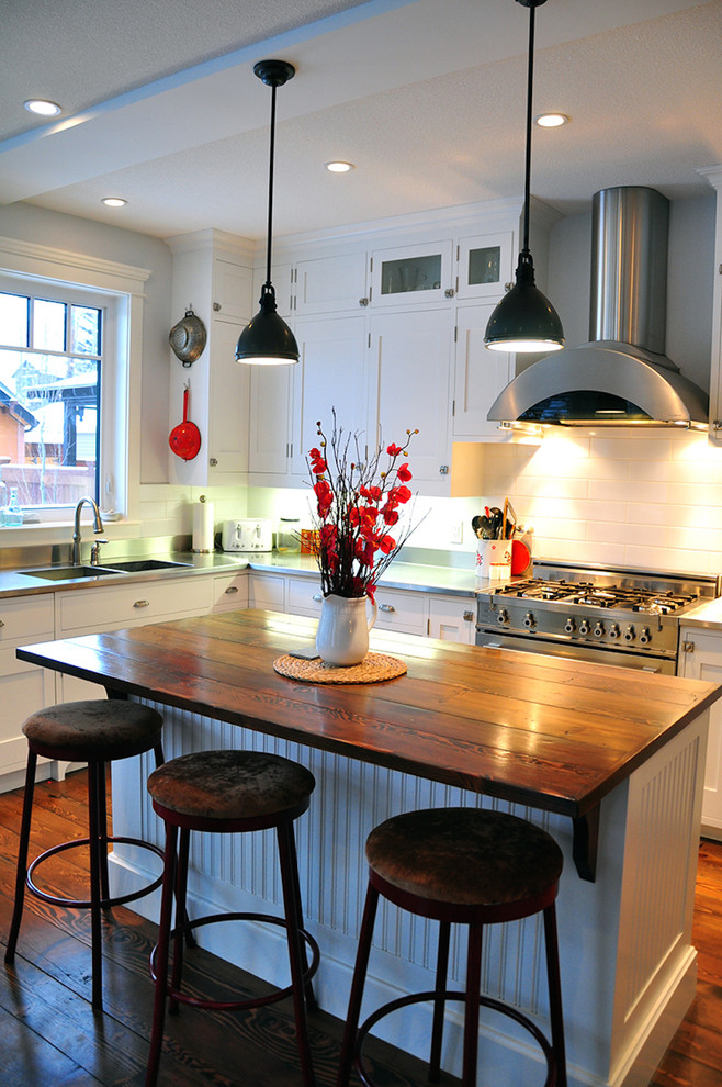 Example of a large l-shaped medium tone wood floor kitchen design in Calgary with white backsplash, stainless steel appliances, a double-bowl sink, beaded inset cabinets, white cabinets, wood countertops and an island