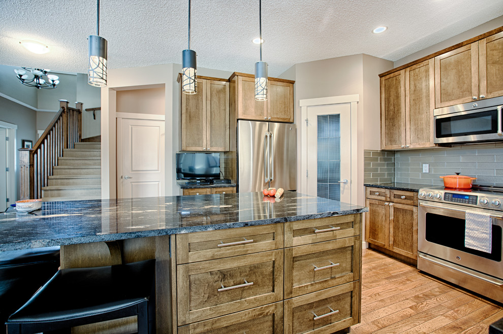 Inspiration for a mid-sized rustic u-shaped medium tone wood floor and brown floor eat-in kitchen remodel in Calgary with an undermount sink, shaker cabinets, medium tone wood cabinets, granite countertops, gray backsplash, glass tile backsplash, stainless steel appliances and an island
