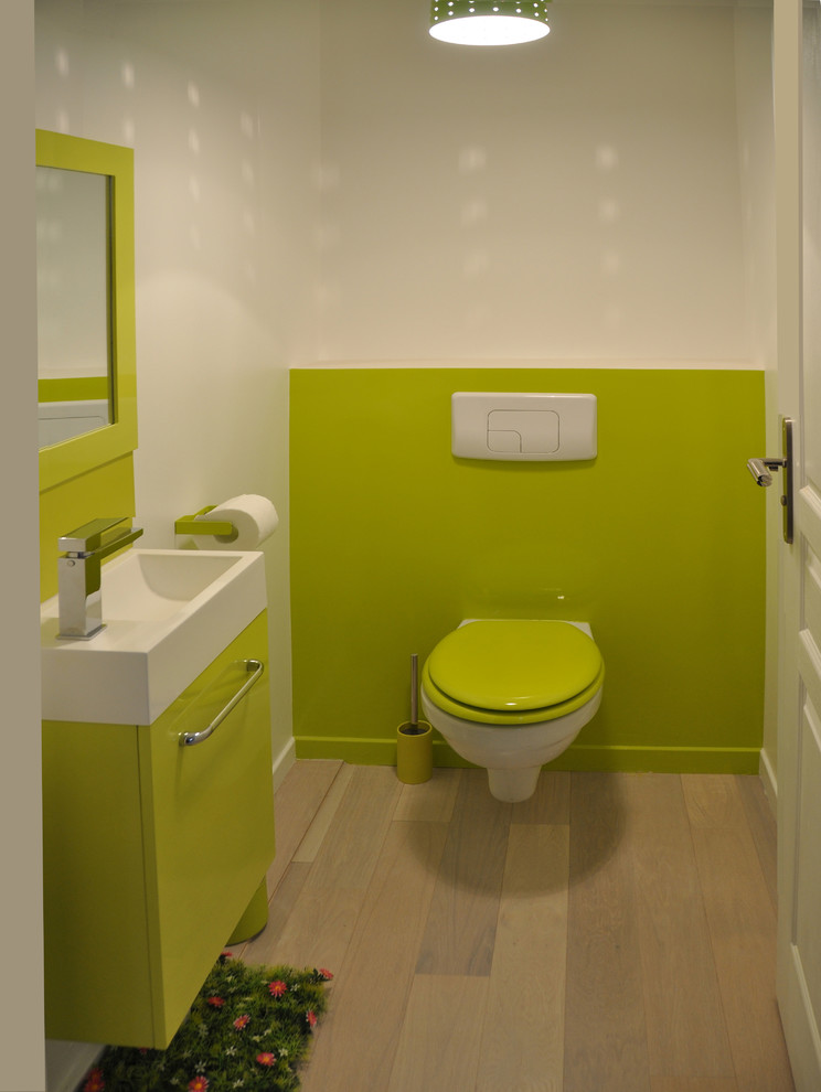 Inspiration for a mid-sized modern powder room in Nantes with green walls, a wall-mount sink, green cabinets, a wall-mount toilet, light hardwood floors and flat-panel cabinets.