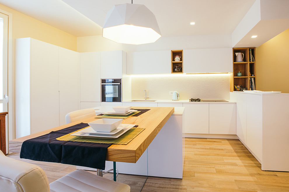 This is an example of a large contemporary u-shaped eat-in kitchen in Bologna with flat-panel cabinets, white cabinets, white splashback, medium hardwood floors, with island, brown floor and black appliances.