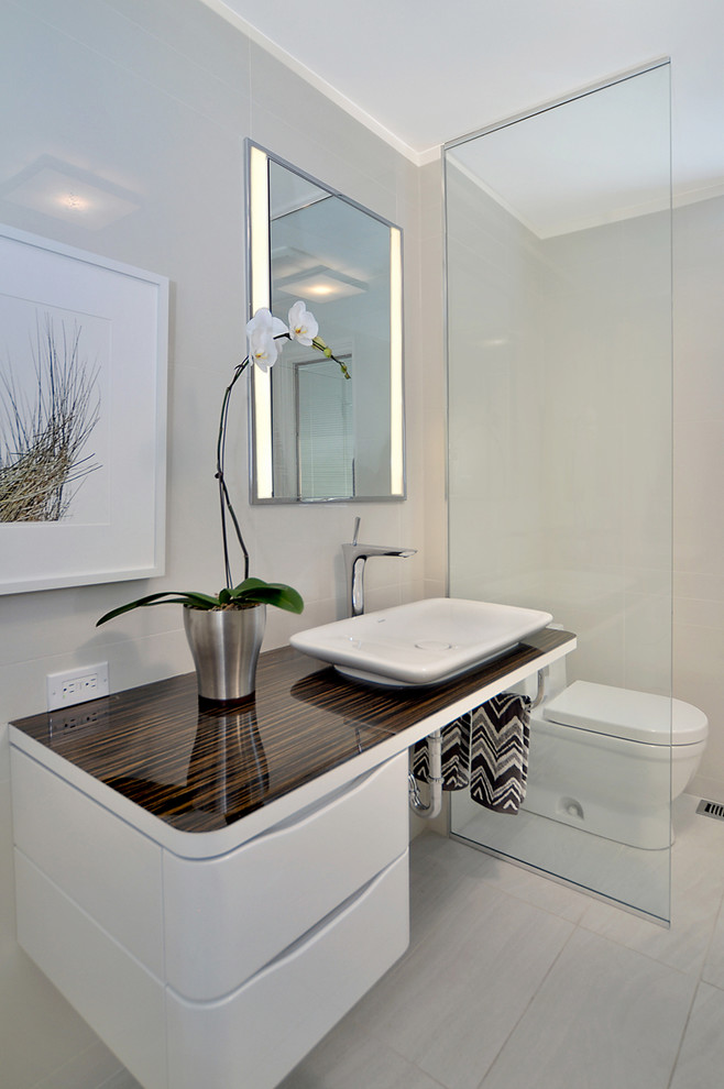 This is an example of a contemporary powder room in Calgary with white cabinets, white tile, grey walls, porcelain floors and brown benchtops.