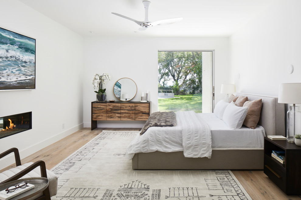 Mid-sized trendy medium tone wood floor and brown floor bedroom photo in Austin with white walls and a ribbon fireplace