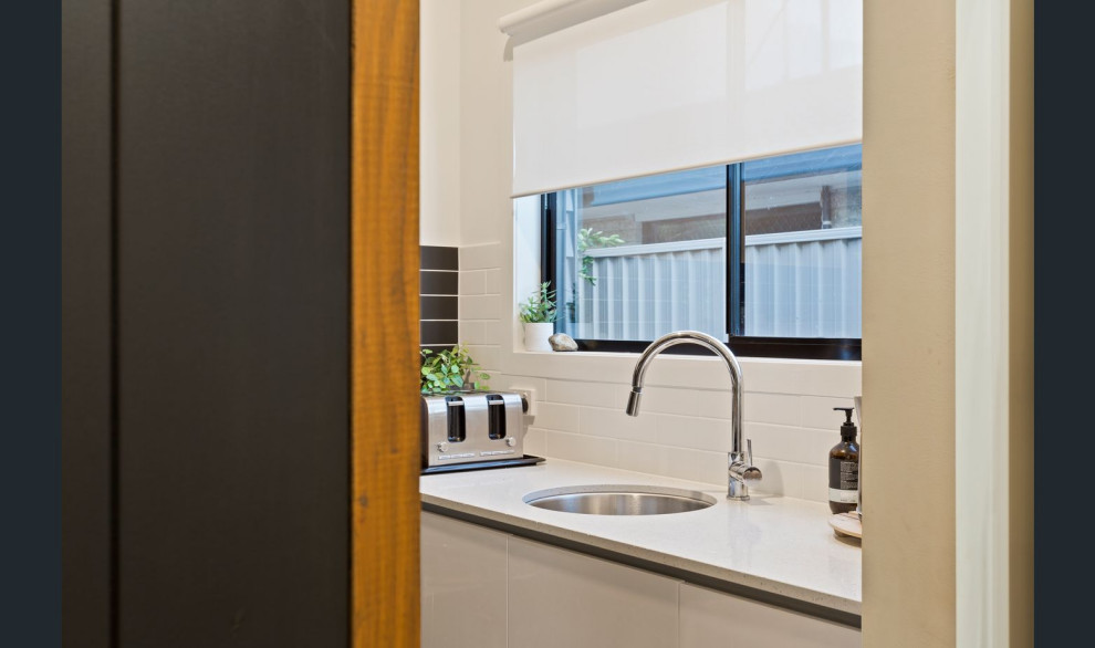 This is an example of a mid-sized contemporary galley open plan kitchen in Gold Coast - Tweed with an undermount sink, flat-panel cabinets, white cabinets, quartz benchtops, brown splashback, subway tile splashback, stainless steel appliances, concrete floors, with island, beige floor and beige benchtop.
