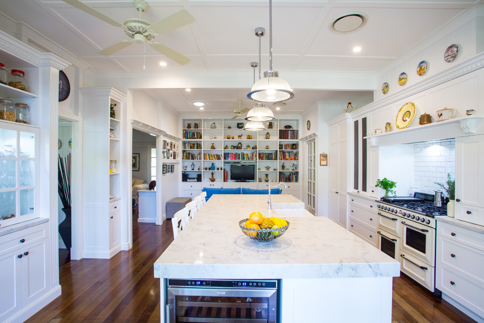 This is an example of a large traditional galley eat-in kitchen in Brisbane with shaker cabinets, white cabinets, white splashback, coloured appliances, with island, a farmhouse sink, solid surface benchtops, subway tile splashback and dark hardwood floors.