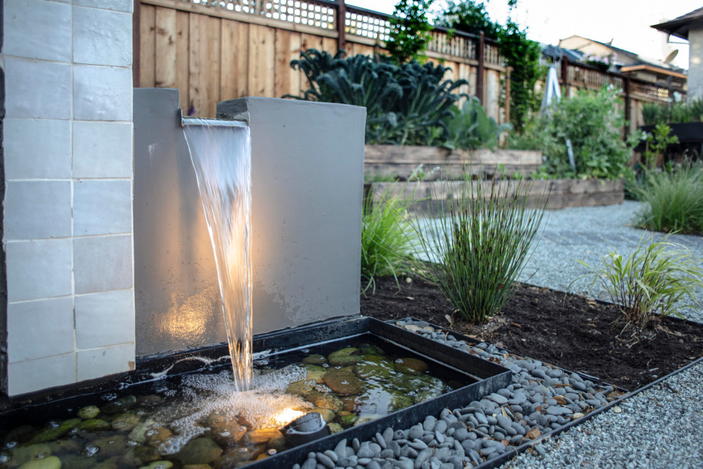 Small contemporary backyard partial sun garden in Other with a water feature and river rock.