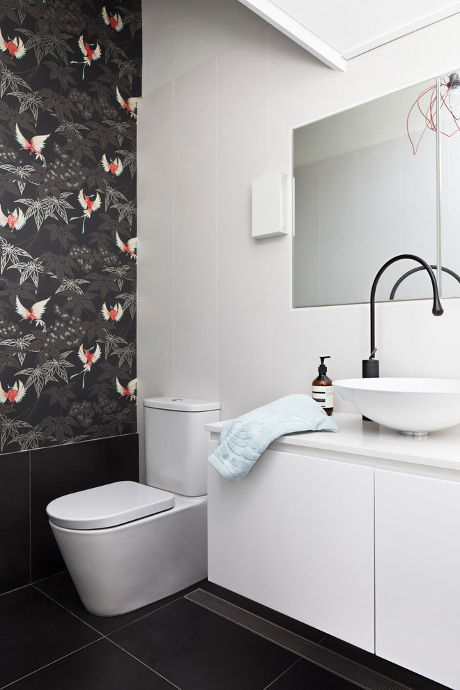 This is an example of a mid-sized eclectic 3/4 bathroom in Sydney with flat-panel cabinets, white cabinets, a one-piece toilet, white tile, ceramic tile, white walls, ceramic floors, a vessel sink, solid surface benchtops and black floor.