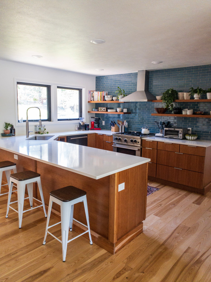Inspiration for a mid-sized midcentury u-shaped kitchen pantry in Other with an undermount sink, flat-panel cabinets, medium wood cabinets, quartz benchtops, blue splashback, subway tile splashback, stainless steel appliances, light hardwood floors, a peninsula, brown floor and white benchtop.