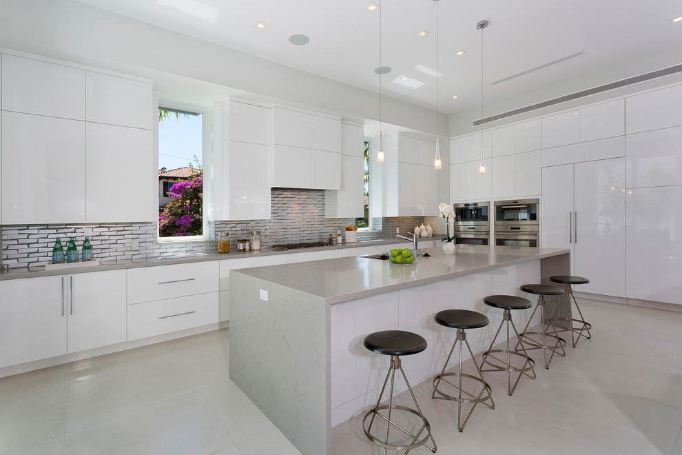 Inspiration for a large contemporary l-shaped open plan kitchen in Miami with an undermount sink, flat-panel cabinets, white cabinets, metallic splashback, stainless steel appliances, with island, grey floor, grey benchtop, marble benchtops, subway tile splashback and porcelain floors.