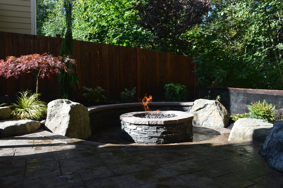 Example of a mid-sized arts and crafts backyard stamped concrete patio design in Seattle with a fire pit and no cover