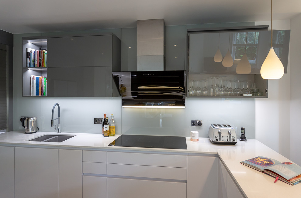 Mid-sized modern u-shaped open plan kitchen in Surrey with an integrated sink, flat-panel cabinets, white cabinets, quartzite benchtops, grey splashback, glass sheet splashback, stainless steel appliances, light hardwood floors, with island, brown floor and white benchtop.
