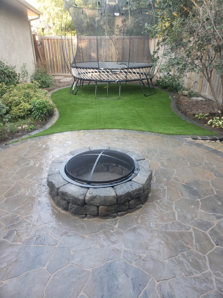 This is an example of a mid-sized rustic shade backyard concrete paver landscaping in Edmonton with a fire pit for summer.