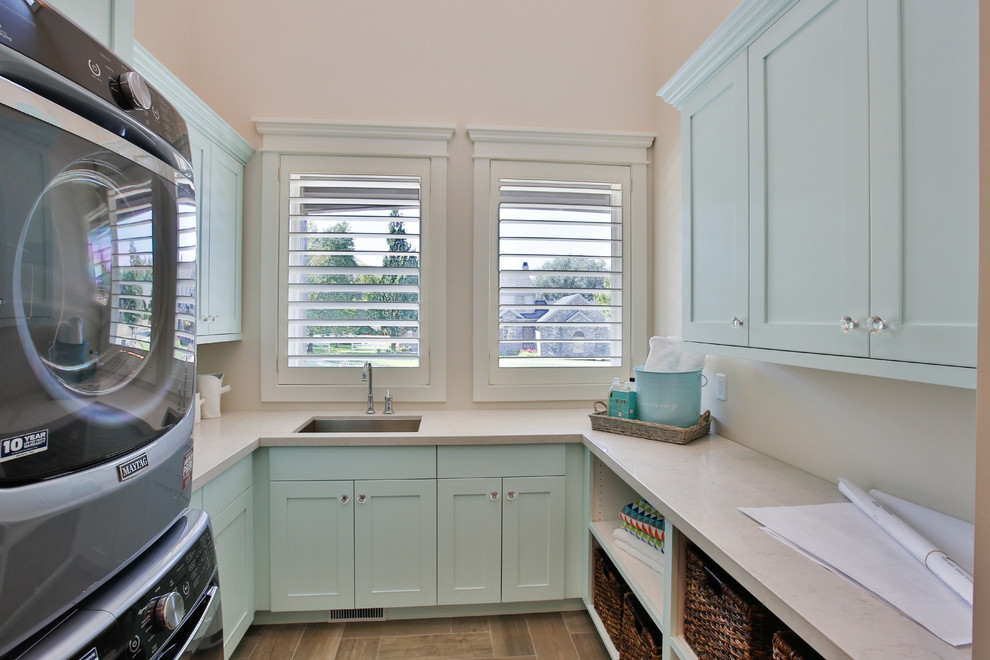 Large transitional u-shaped dedicated laundry room in Salt Lake City with an undermount sink, shaker cabinets, blue cabinets, white walls, a stacked washer and dryer, quartzite benchtops and porcelain floors.