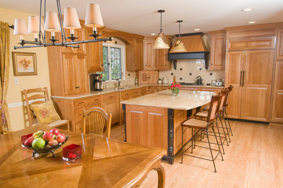 This is an example of a traditional eat-in kitchen in Philadelphia with raised-panel cabinets, medium wood cabinets, beige splashback, panelled appliances, an undermount sink, granite benchtops, light hardwood floors, with island and beige benchtop.