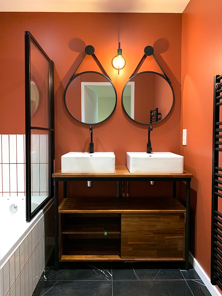 Пример оригинального дизайна: главная ванная комната среднего размера в стиле фьюжн с плоскими фасадами, темными деревянными фасадами, полновстраиваемой ванной, душем над ванной, раздельным унитазом, белой плиткой, керамической плиткой, оранжевыми стенами, накладной раковиной, столешницей из дерева, черным полом, душем с распашными дверями, коричневой столешницей, тумбой под две раковины, напольной тумбой и мраморным полом