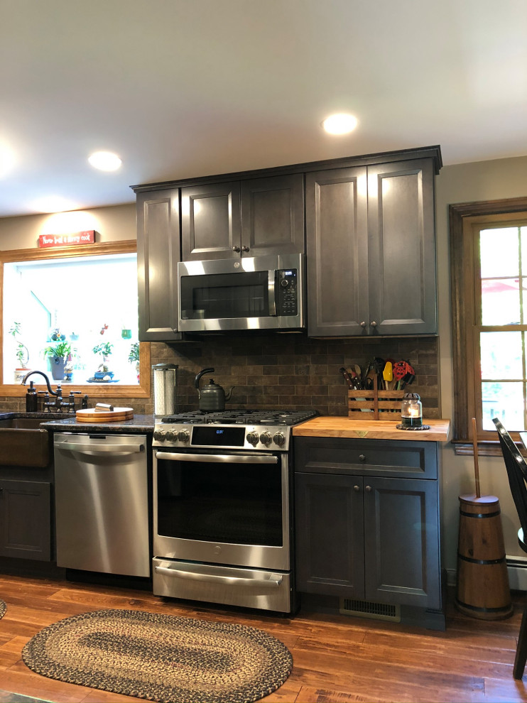 Inspiration for a mid-sized traditional galley eat-in kitchen in Bridgeport with a farmhouse sink, raised-panel cabinets, brown cabinets, granite benchtops, brown splashback, stone tile splashback, stainless steel appliances, dark hardwood floors, no island, brown floor and brown benchtop.
