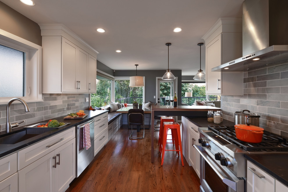 Photo of a mid-sized midcentury galley eat-in kitchen in Seattle with shaker cabinets, white cabinets, soapstone benchtops, green splashback, stainless steel appliances, medium hardwood floors, a farmhouse sink, with island and brown floor.