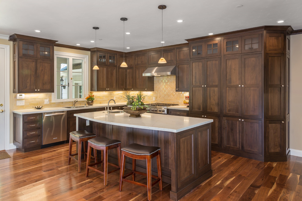 This is an example of a large arts and crafts l-shaped eat-in kitchen in San Francisco with an undermount sink, beaded inset cabinets, dark wood cabinets, marble benchtops, yellow splashback, ceramic splashback, stainless steel appliances, medium hardwood floors and with island.