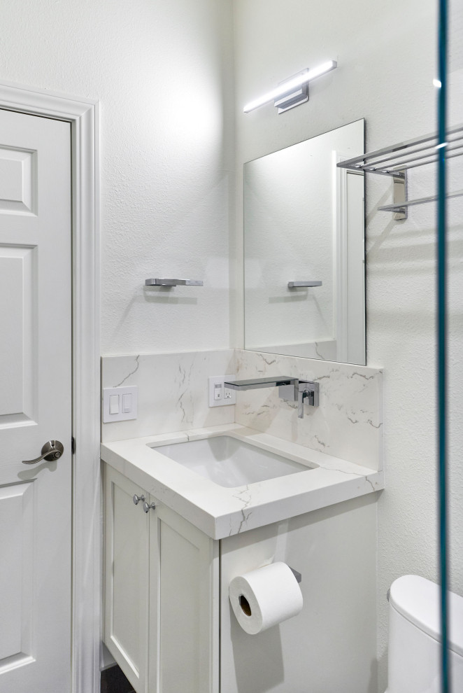 Inredning av ett klassiskt litet vit vitt badrum med dusch, med luckor med infälld panel, vita skåp, en dusch i en alkov, en toalettstol med hel cisternkåpa, vit kakel, porslinskakel, vita väggar, klinkergolv i porslin, ett undermonterad handfat, bänkskiva i kvarts, brunt golv och dusch med gångjärnsdörr