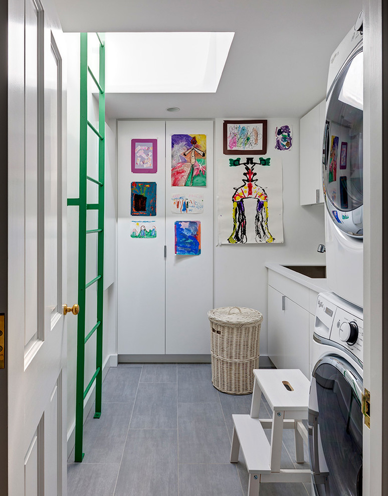 Design ideas for a contemporary single-wall dedicated laundry room in New York with white cabinets, white walls, a stacked washer and dryer, grey floor and flat-panel cabinets.