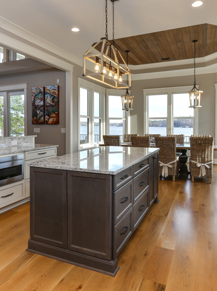 Design ideas for a mid-sized transitional u-shaped open plan kitchen in Raleigh with a farmhouse sink, recessed-panel cabinets, white cabinets, granite benchtops, white splashback, stainless steel appliances, light hardwood floors, with island and white benchtop.