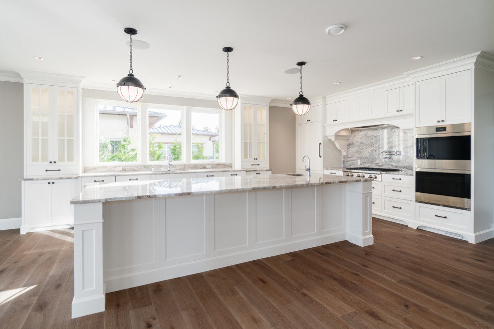 Large traditional u-shaped eat-in kitchen in Vancouver with an undermount sink, recessed-panel cabinets, white cabinets, limestone benchtops, multi-coloured splashback, stone slab splashback, stainless steel appliances, medium hardwood floors, with island, brown floor and multi-coloured benchtop.