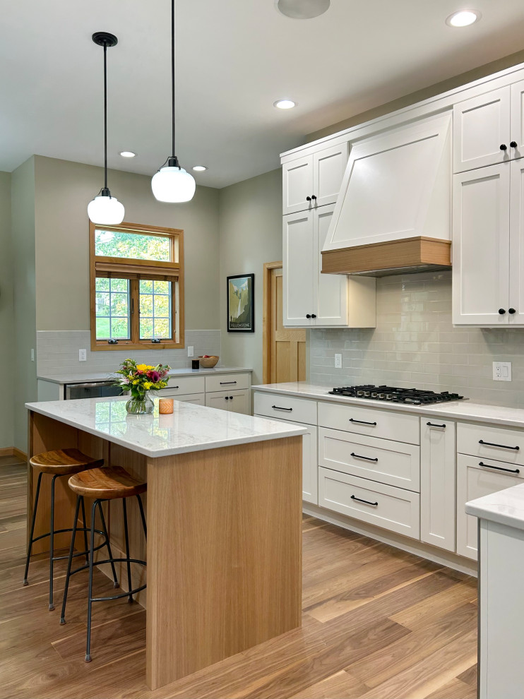 Mid-sized transitional l-shaped medium tone wood floor and brown floor open concept kitchen photo with an undermount sink, flat-panel cabinets, white cabinets, quartz countertops, gray backsplash, ceramic backsplash, stainless steel appliances, an island and white countertops