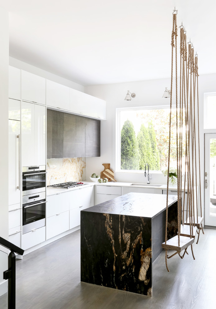 Inspiration for a contemporary l-shaped eat-in kitchen in New York with an undermount sink, flat-panel cabinets, white cabinets, marble benchtops, white splashback, marble splashback, stainless steel appliances, medium hardwood floors, with island, brown floor and black benchtop.