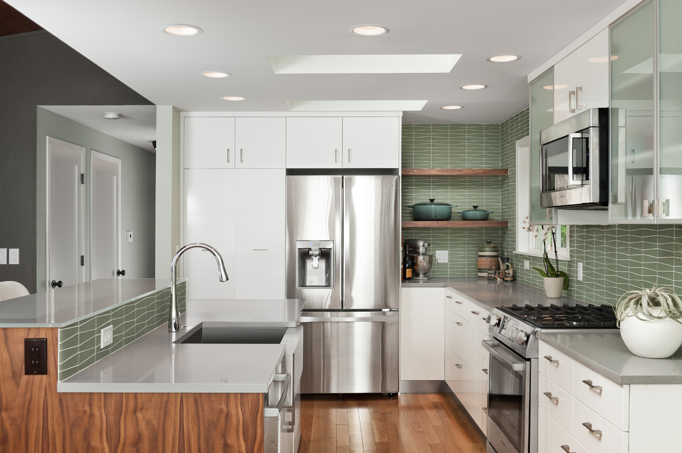 Inspiration for a mid-sized midcentury eat-in kitchen in Portland with a farmhouse sink, flat-panel cabinets, medium wood cabinets, quartz benchtops, green splashback, glass tile splashback, stainless steel appliances, medium hardwood floors, with island, brown floor and grey benchtop.